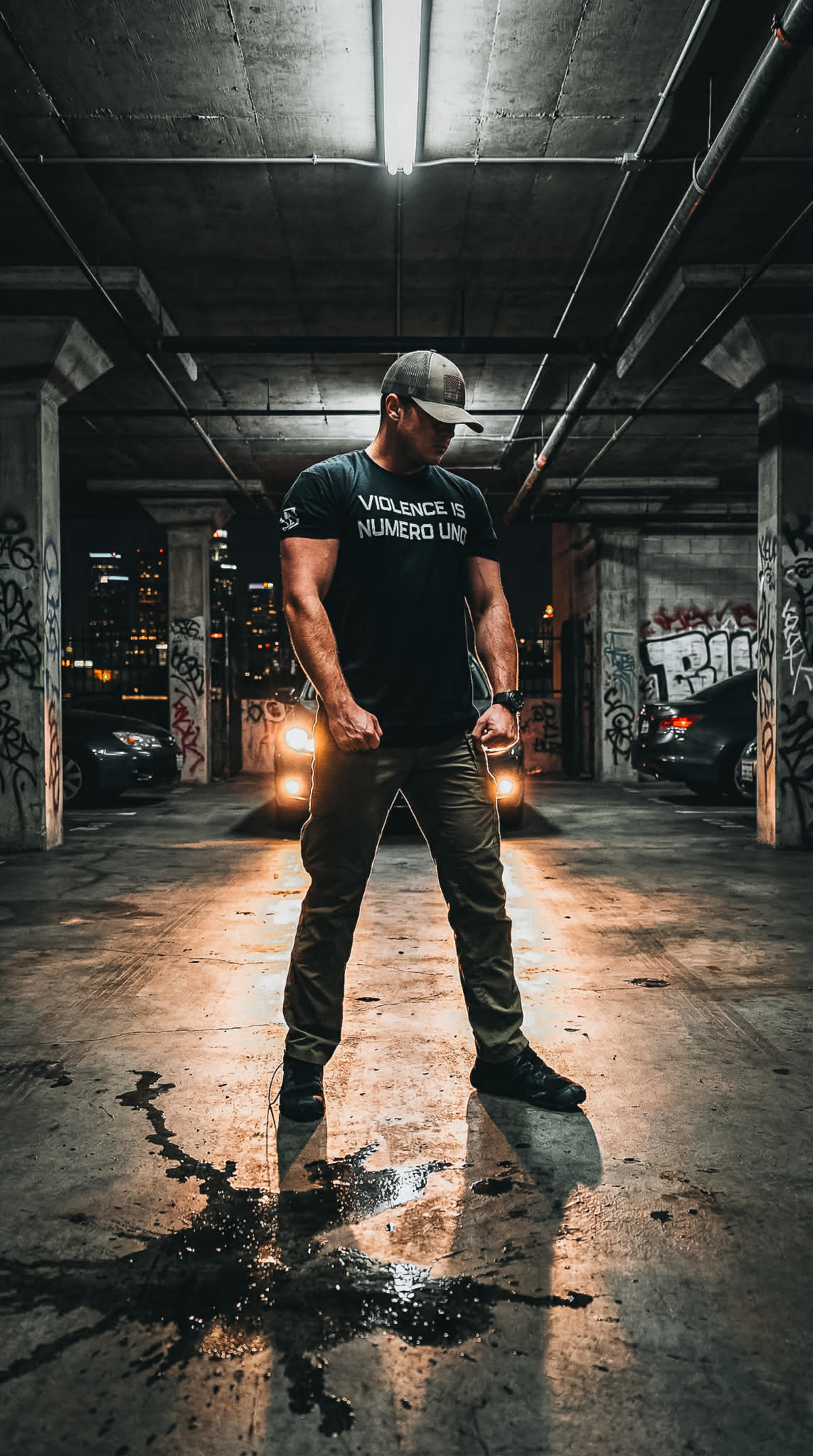 Man standing in a dark, urban parking garage wearing a black t-shirt with text.